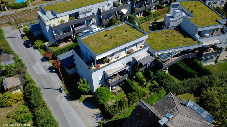 Luftaufnahme moderner Wohngebäude mit begrünten Dächern, Balkonen und gepflegten Gärten in einer Wohnsiedlung.
