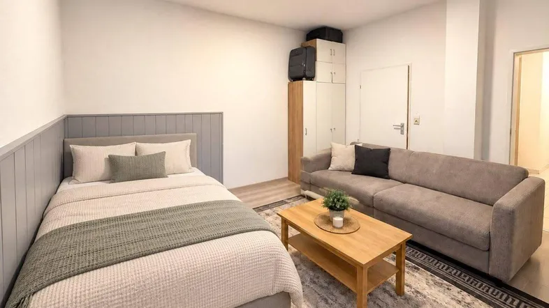 Helles Schlafzimmer mit Bett, Sofa und Holztisch, ideal für ein Studio-Apartment.