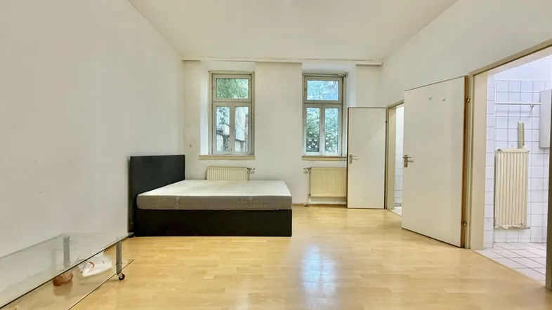 Helles Schlafzimmer mit Holzboden, zwei Fenstern und Zugang zu einem weiteren Raum.
