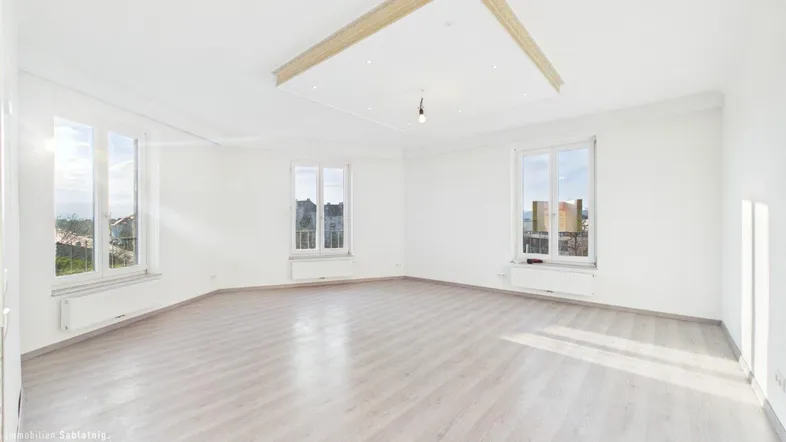 Helles, leeres Zimmer mit hellem Laminatboden und dekorativer Deckenbeleuchtung, bereit zur Einrichtung.