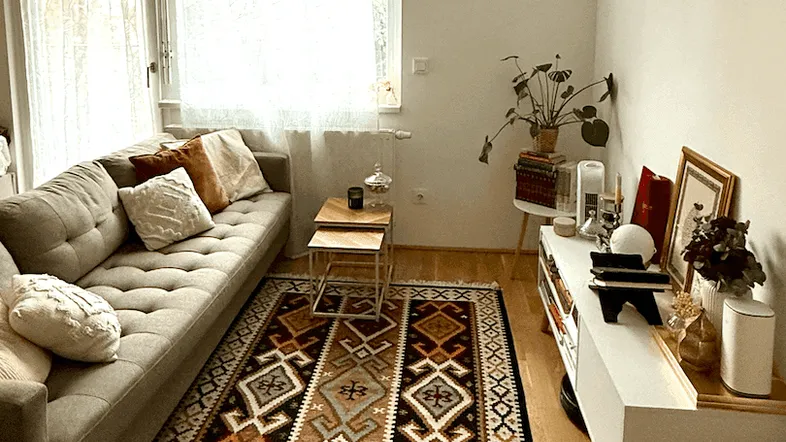 Helles Wohnzimmer mit beigem Sofa, gemustertem Teppich und Holzboden, gut beleuchtet.
