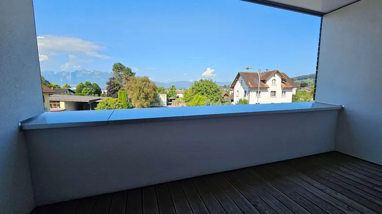 Heller Balkon mit Holzboden und weitem Blick auf die umliegende Landschaft und Berge.