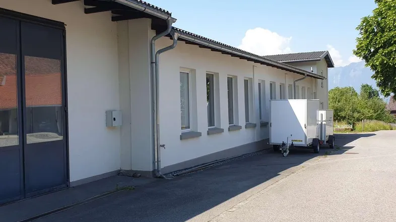Außenansicht eines Gewerbegebäudes mit weißer Fassade, großen Fenstern und Blick auf die Berge im Hintergrund.
