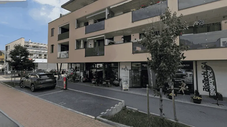 Modernes Mehrfamilienhaus mit Geschäften im Erdgeschoss und Balkonen in einer städtischen Umgebung.