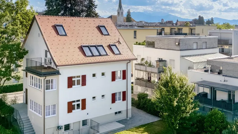 Luftaufnahme des Anwesens mit großem Garten, umliegenden Häusern und Bergblick im Hintergrund.
