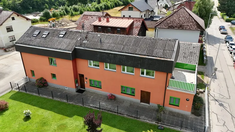 Orangefarbenes Mehrfamilienhaus mit grünen Fensterrahmen und einem kleinen Vorgarten.