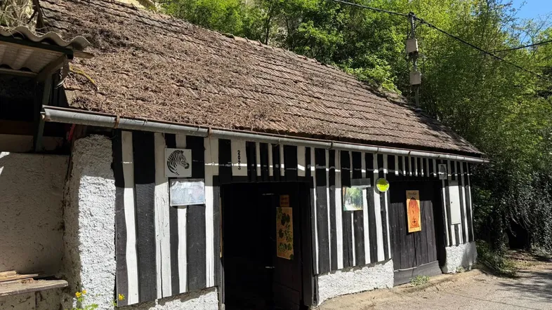 Rustikales Gebäude mit schwarz-weiß gestreifter Fassade und traditionellem Strohdach, umgeben von üppigem Grün.