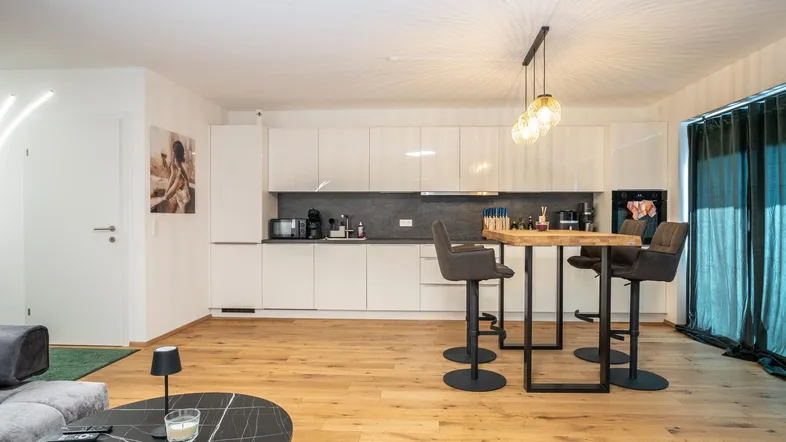 Offener Wohnbereich mit moderner Küche, Bartresen und bequemer Couch im Hintergrund.