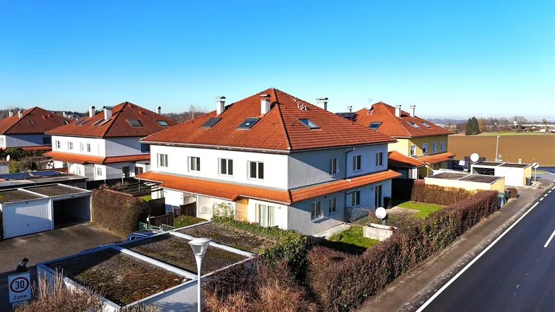 Luftaufnahme einer Wohnsiedlung mit Reihenhäusern, roten Dächern und Garagen in ländlicher Umgebung.