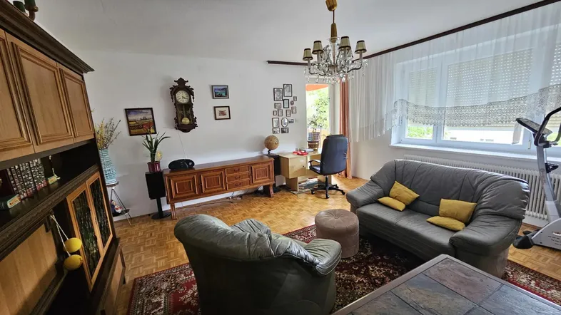 Helles Wohnzimmer mit Parkettboden, Ledersofa, Schreibtisch und einem großen Fenster.