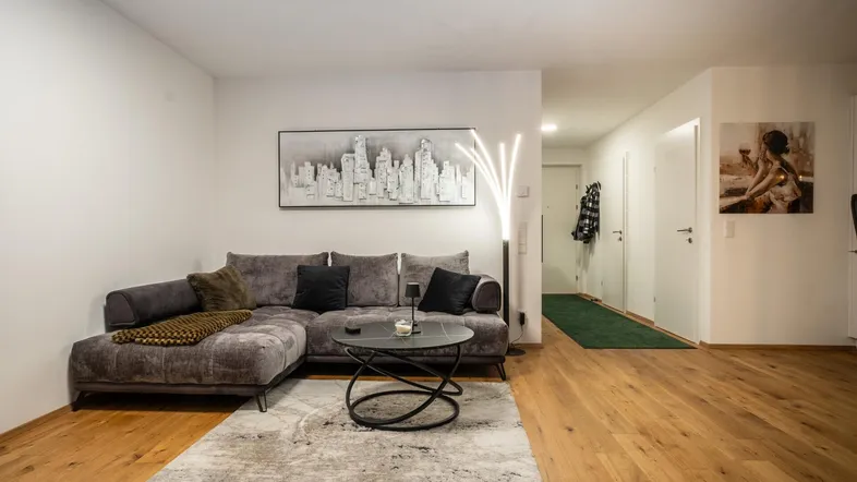 Geräumiges Wohnzimmer mit Holzboden, bequemer Eckcouch und Blick in den Flur.