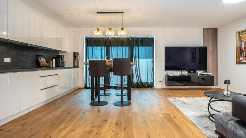 Heller offener Wohnbereich mit integrierter Küche, Bartresen und Zugang zum Balkon.
