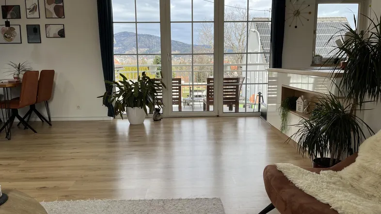 Helles, offenes Wohn-Esszimmer mit großen Fenstern, Holzboden und Bergblick.