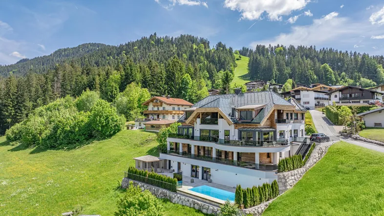 Luxuriöse Villa in alpiner Landschaft mit Bergblick und Außenpool, umgeben von grünen Hügeln.