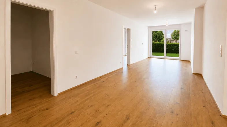 Helles, leeres Zimmer mit Holzboden und großen Fenstern, die Zugang zum Außenbereich bieten.