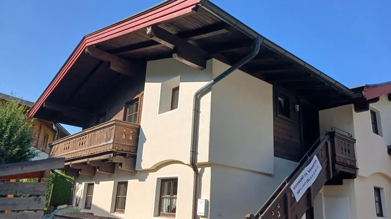 Traditionelles Haus im alpinen Stil mit Holzbalkonen und weißer Fassade unter blauem Himmel.
