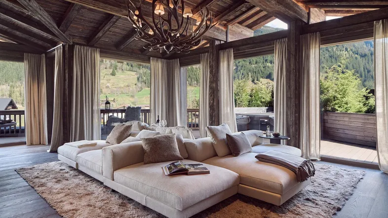 Luxuriöses Wohnzimmer mit Holzbalkendecke, großem Sofa und Panoramafenstern mit Bergblick.