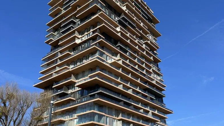 Modernes Hochhaus mit vielen Balkonen und Terrassen in städtischer Umgebung.