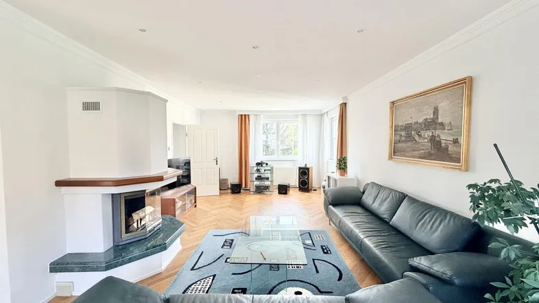 Geräumiges Wohnzimmer mit Fischgrätparkett, Kamin und bequemen Ledersofas, ideal für entspannte Abende.