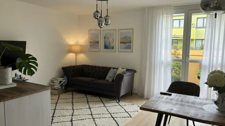 Helles Wohn- und Esszimmer mit modernem Sofa, Esstisch und Zugang zum Balkon.