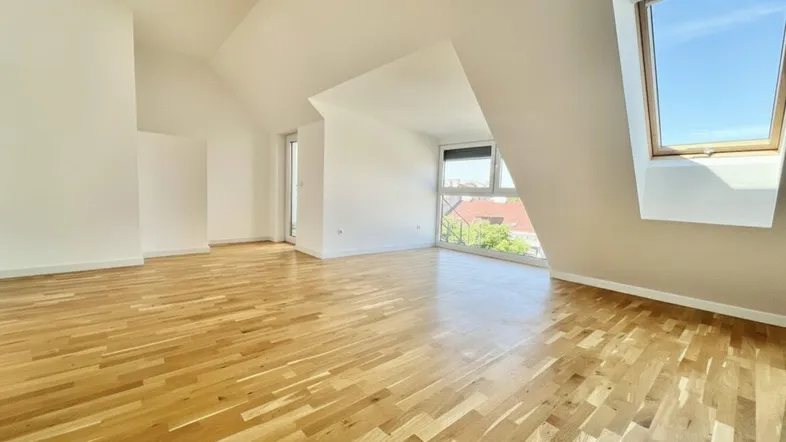 Helles Dachgeschosszimmer mit Holzboden und großen Fenstern, die viel Tageslicht hereinlassen.