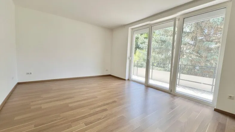 Heller Wohnraum mit großen Fenstern, Holzboden und Blick ins Grüne.