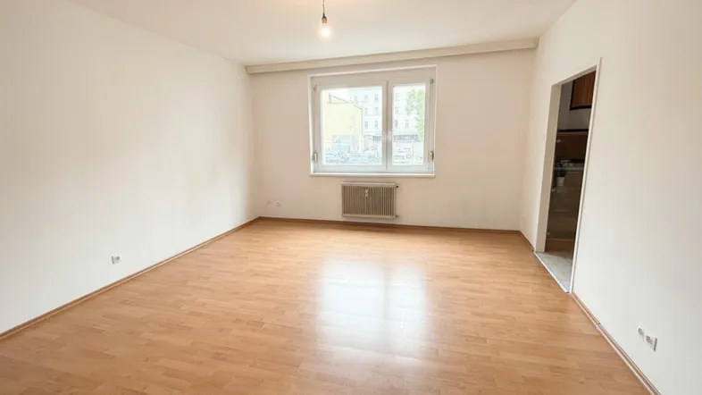 Helles Wohnzimmer mit Laminatboden und einem Fenster, bereit zur individuellen Gestaltung.