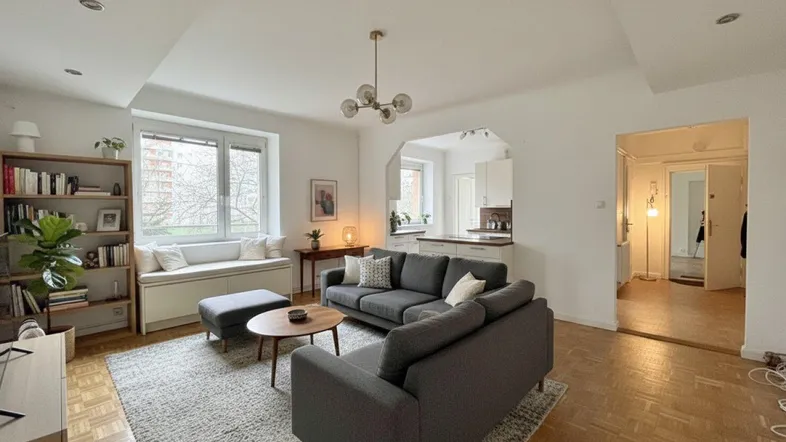 Helles Wohnzimmer mit Parkettboden, gemütlicher Sitzecke und offenem Übergang zur Küche.