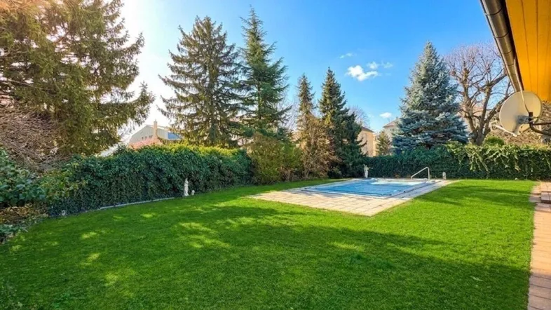 Großer Gartenbereich mit gepflegtem Rasen, altem Baumbestand und einem abgedeckten Swimmingpool.
