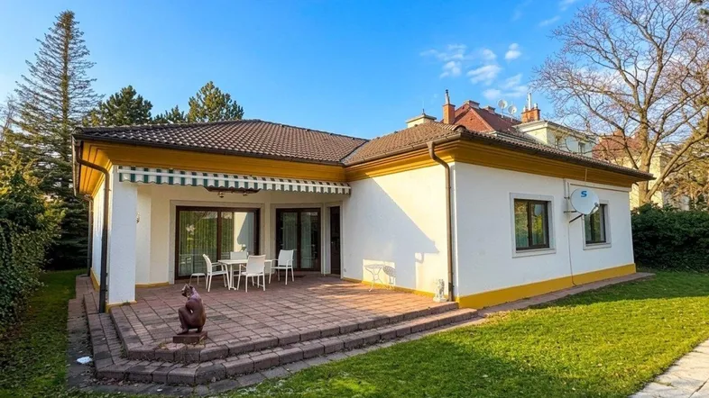 Einfamilienhaus mit sonniger Terrasse, Gartenmöbeln und gepflegtem Rasenbereich unter blauem Himmel.