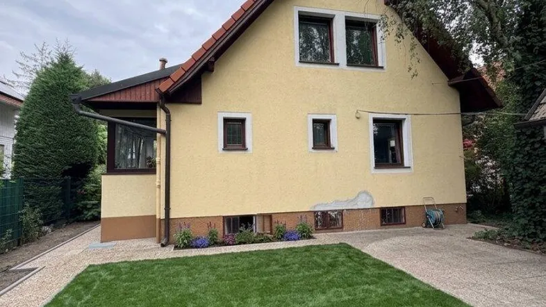 Gelbes Einfamilienhaus mit Satteldach, gepflegtem Vorgarten und Zufahrt.
