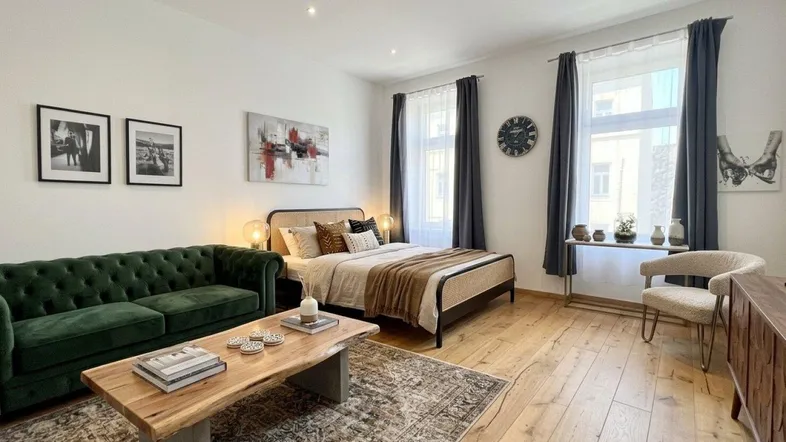 Helles Wohnzimmer mit Holzboden, bequemer Couch und einem Bett im Hintergrund, modern eingerichtet.