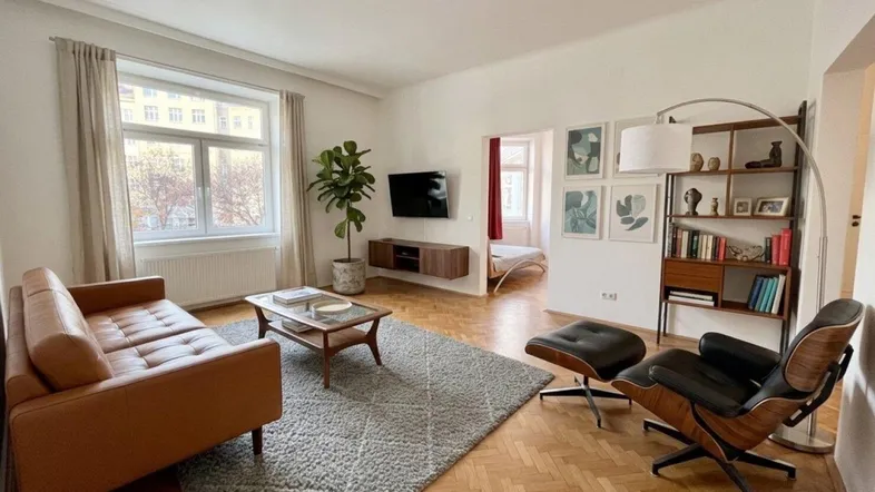 Helles Wohnzimmer mit Fischgrätparkett, Ledersofa, Bücherregal und Blick nach draußen.