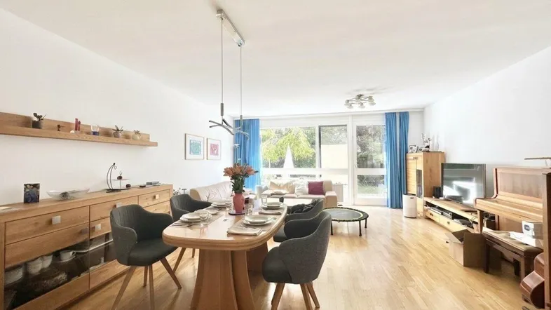 Geräumiger Wohn-Essbereich mit Holzboden, großem Esstisch und Blick ins Grüne durch große Fenster.