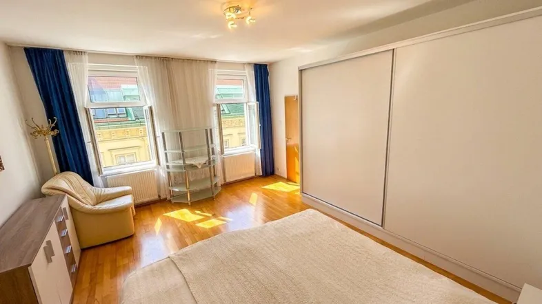 Helles Schlafzimmer mit Parkettboden, großen Fenstern und einem praktischen Einbauschrank.
