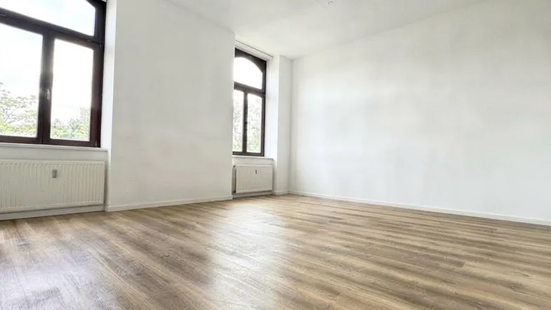 Heller Wohnraum mit modernem Laminatboden, hohen Fenstern und Heizkörpern.