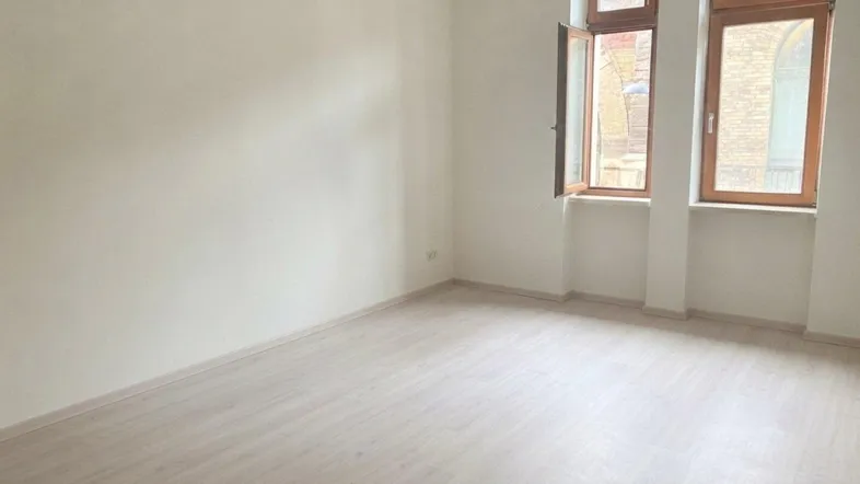 Helles Zimmer mit hellem Laminatboden und großen Fenstern, ideal als Wohn- oder Schlafzimmer nutzbar.