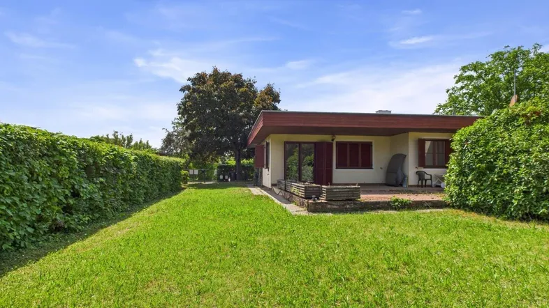 Ansicht des Hauses von der Gartenseite mit großer Rasenfläche und einer kleinen Terrasse.