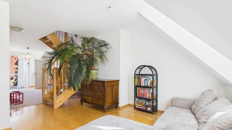 Gemütliches Wohnzimmer im Dachgeschoss mit Sofa, Bücherregal und sichtbarer Holztreppe.