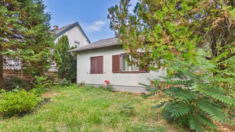 Kleines Einfamilienhaus mit grünem Garten und Bäumen in ländlicher Umgebung.