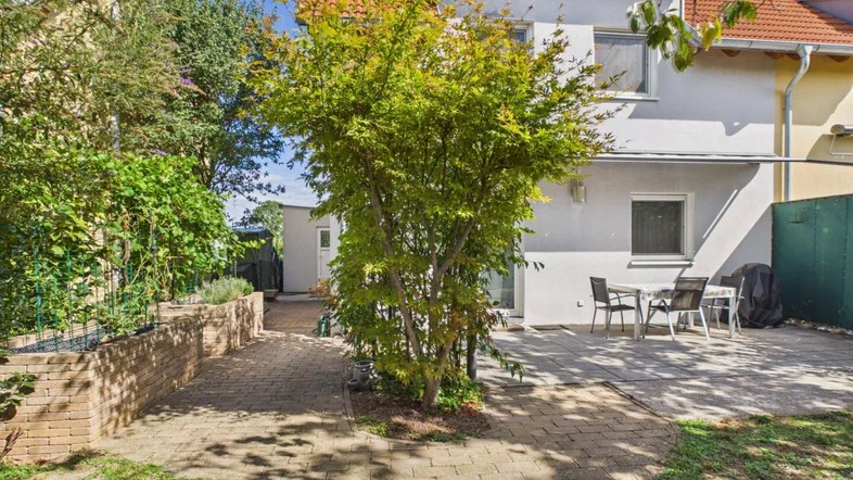 Hinterhof mit gepflasterter Terrasse, Gartenmöbeln und einem Baum, ideal für Entspannung im Freien.