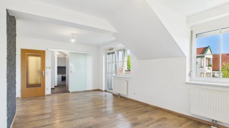 Helles Wohnzimmer mit Holzboden, weißen Wänden und Zugang zur Küche durch eine Schiebetür.