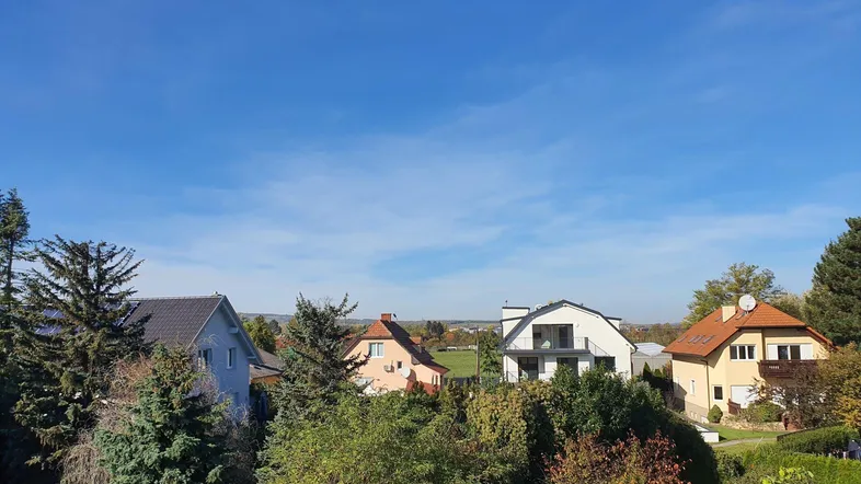 Blick über eine Wohnsiedlung mit verschiedenen Häusern und viel Grün unter blauem Himmel.