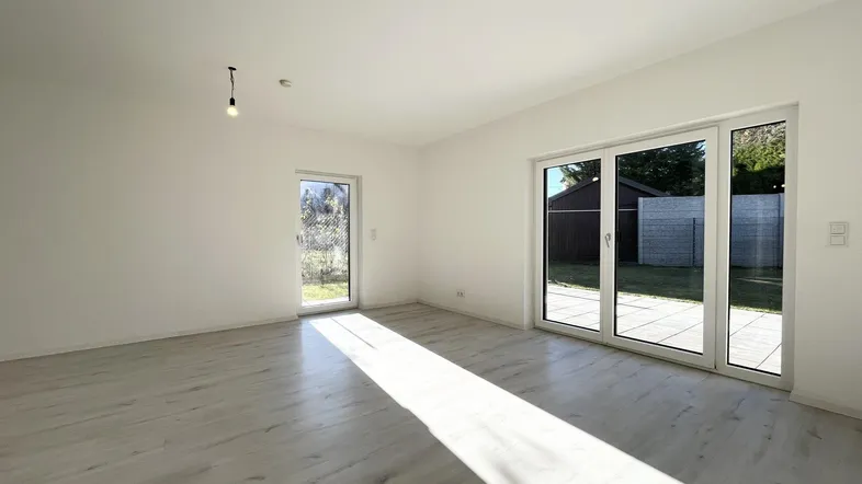 Helles, leeres Wohnzimmer mit Laminatboden und großen Fenstern zum Garten.