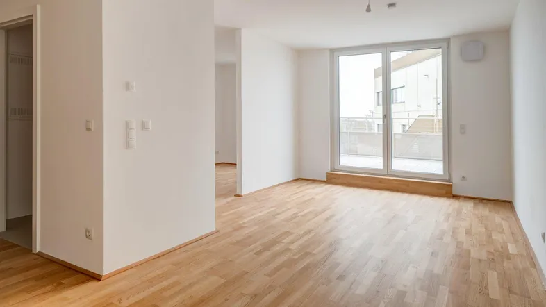 Helles, leeres Zimmer mit Parkettboden und Zugang zu einem Balkon, ideal für einen Wohnbereich.