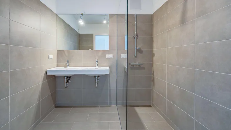 Modernes Badezimmer mit Doppelwaschbecken, großer Duschkabine und hellen Fliesen.