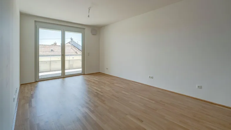 Helles, leeres Zimmer mit Holzboden und Zugang zu einem Balkon, ideal als Wohn- oder Schlafzimmer.