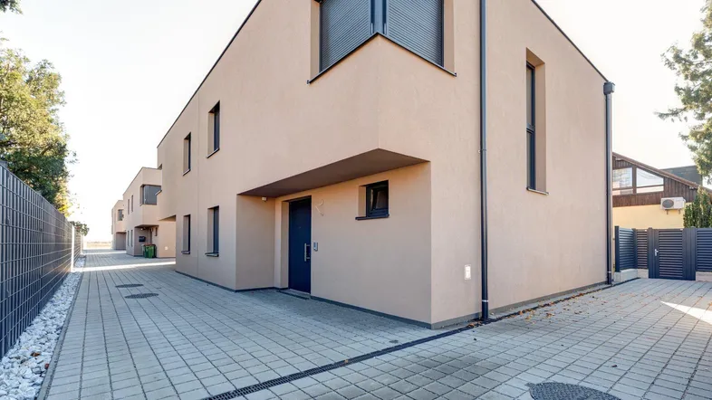 Moderne Reihenhäuser mit gepflastertem Zugangsbereich und dunklen Fensterläden.