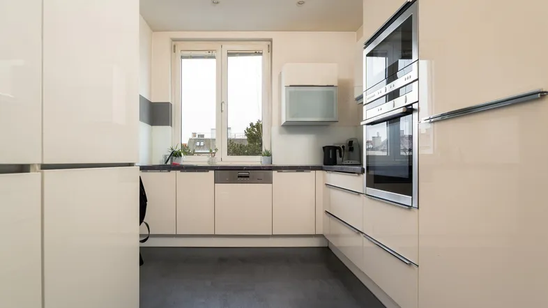 Moderne Küche mit glänzenden cremefarbenen Fronten, integrierten Geräten und einem Fenster über der Spüle.