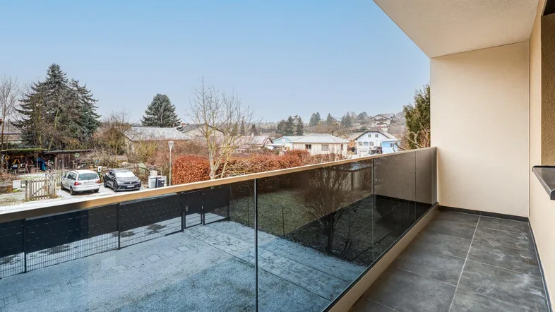 Moderner Balkon mit Glasgeländer und Blick auf die verschneite Umgebung und parkende Autos.